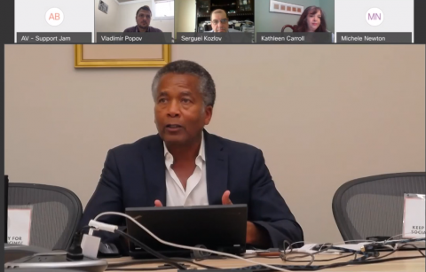 A screenshot of a virtual meeting with a man talking and smaller videos of participants at the top of his video stream