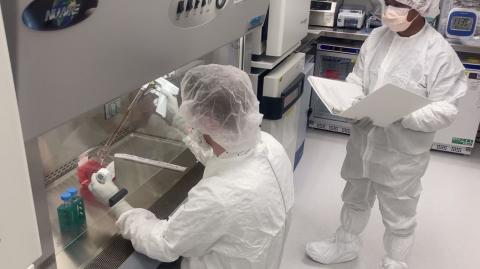 Two scientists in full protective gear stand at a 