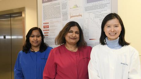 Monika Mehta, research and development manager; Jyoti Shetty, Illumina laboratory manager; and Yongmei Zhao, bioinformatics manager, from the Sequencing Facility stand together in front of a scientific poster.