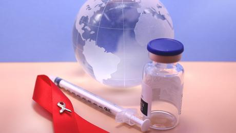HIV ribbon next to syringe and vial in front of glass globe